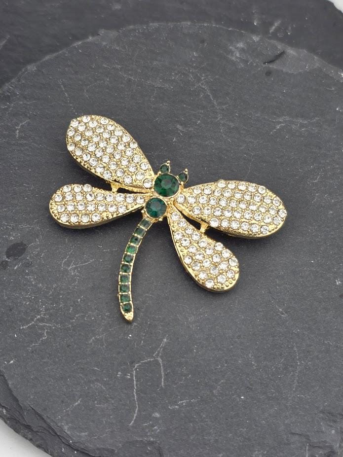 A decorative white frame with a gold-colored brooch featuring a diamond-encrusted dragonfly design.
