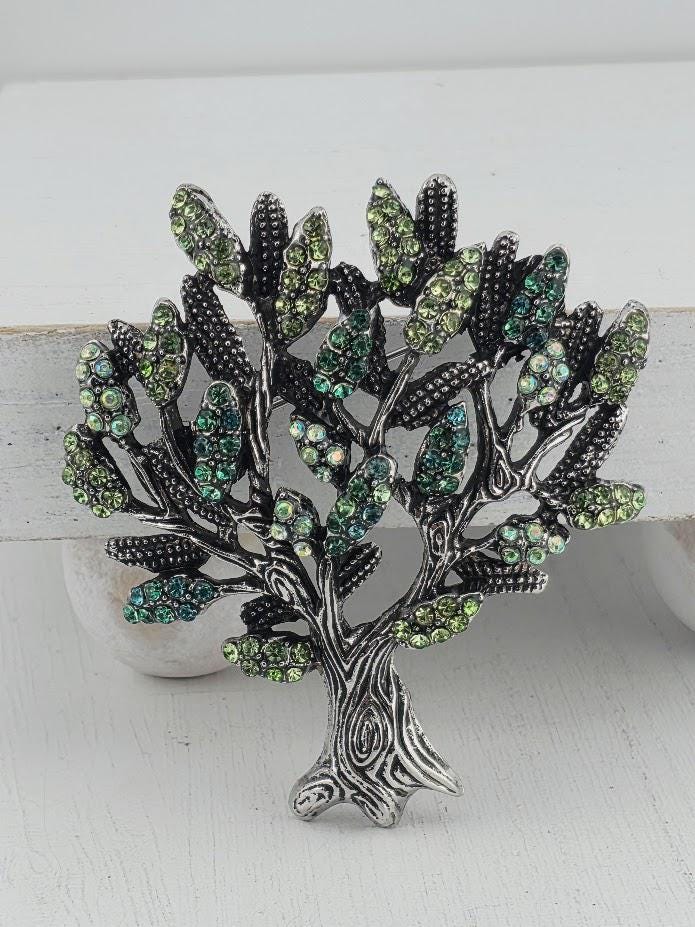 A decorative brooch in the shape of a tree, adorned with green and silver rhinestones or crystals.