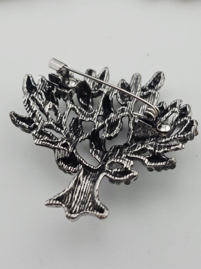 A decorative metal pin in the shape of a tree, with intricate details and a metallic sheen.