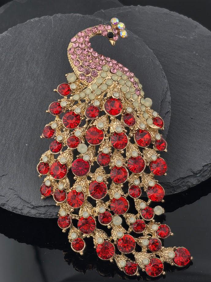 A decorative brooch in the shape of a peacock, adorned with red and gold gemstones.