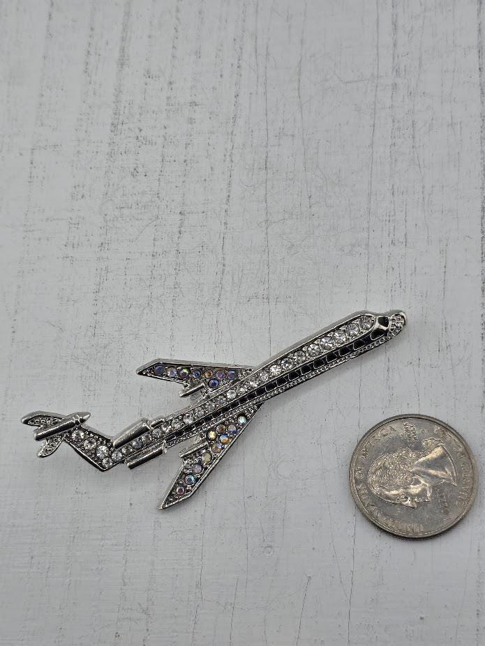 A silver airplane brooch with rhinestones is placed next to a US quarter on a white surface.