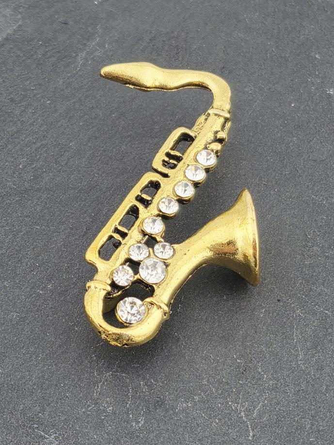 A gold saxophone brooch with rhinestones on a gray surface.