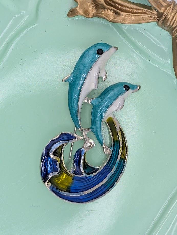 A decorative piece featuring two blue and white dolphins leaping out of a wave-like shape.