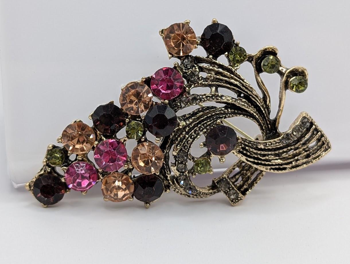 A decorative brooch with a floral design, featuring a variety of colorful gemstones including pink, green, and brown stones.