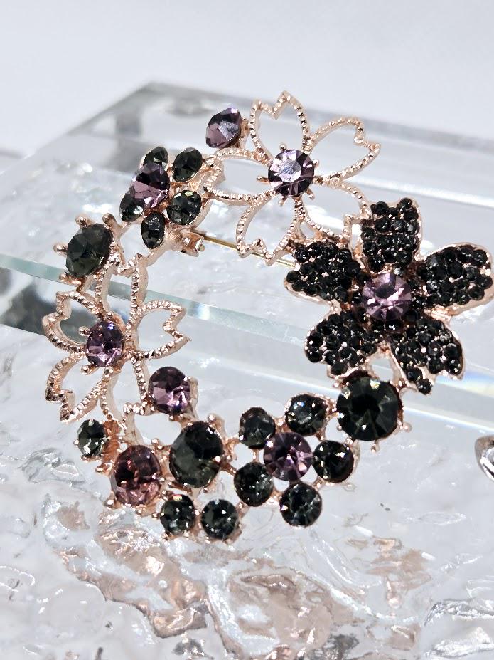 A decorative brooch with a floral design, featuring a combination of black and purple gemstones.