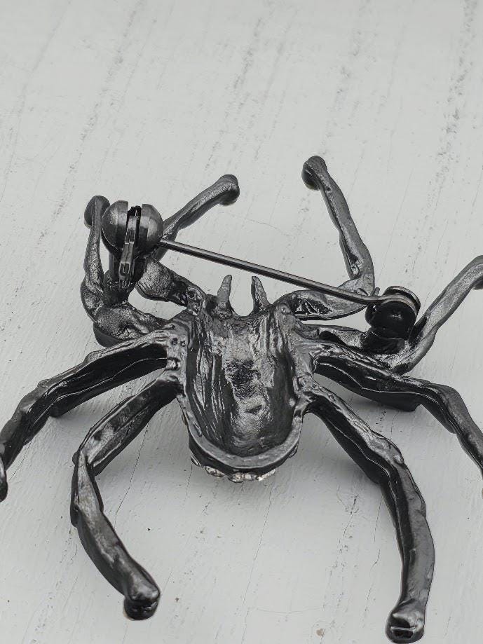 A close-up view of a shiny, metallic spider-like brooch or pin with a textured surface.