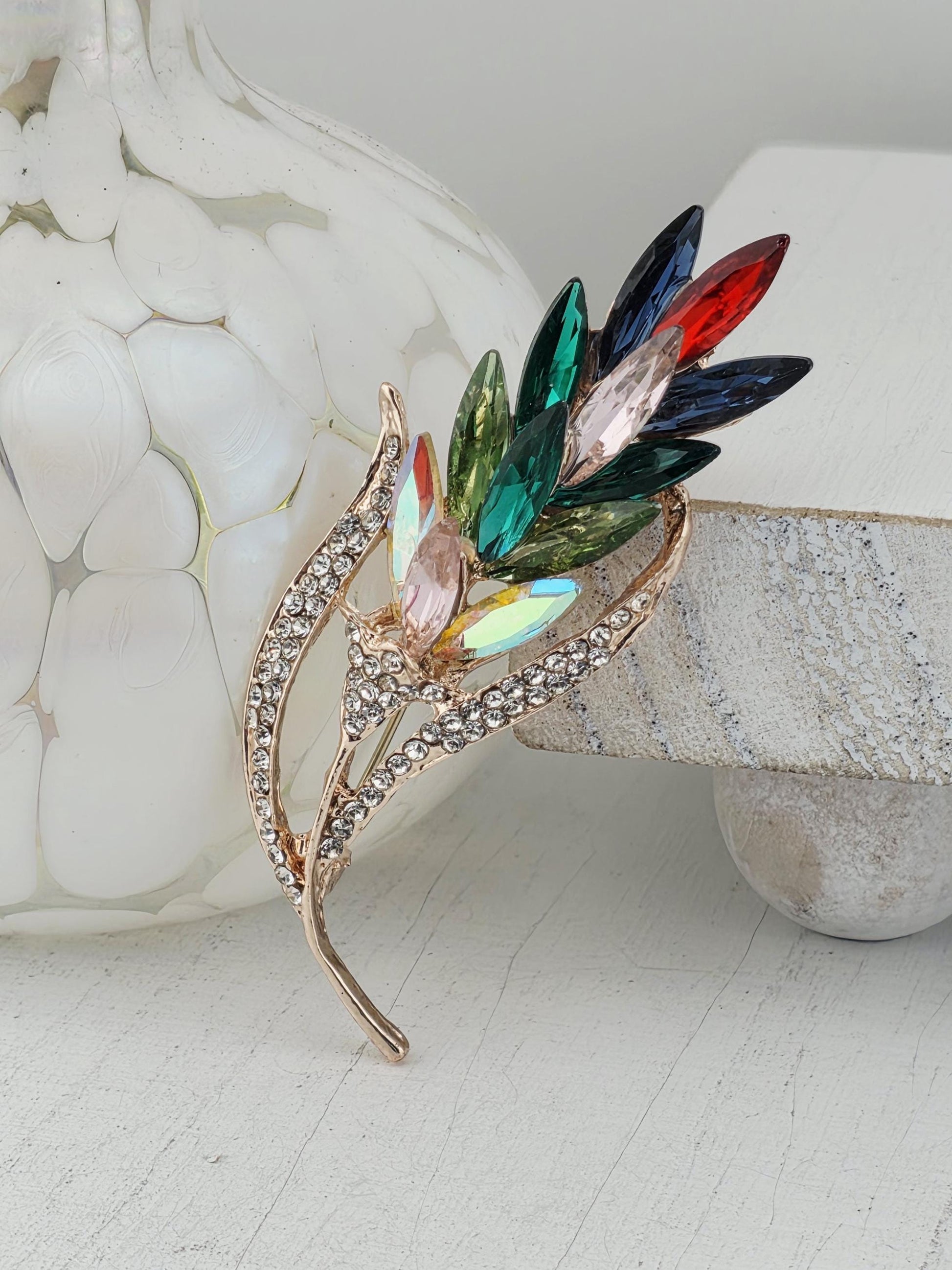 A decorative brooch with a leaf-like design and colorful gemstones.