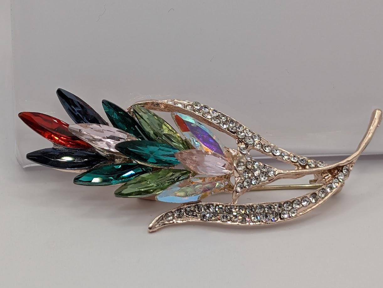 A decorative brooch with a leaf-like design, featuring a variety of colorful gemstones.
