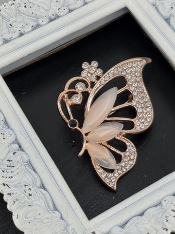 A decorative brooch in the shape of a butterfly, adorned with rhinestones, is displayed within a white ornate frame.
