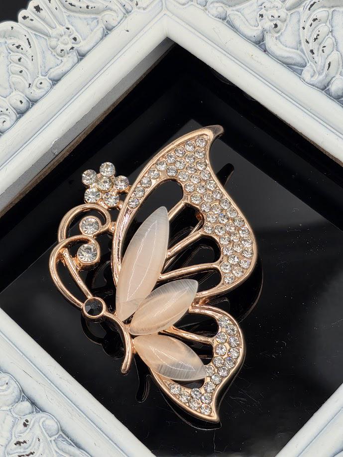 A decorative brooch in the shape of a butterfly, adorned with small diamonds and a flower-like design, is displayed against a black background.