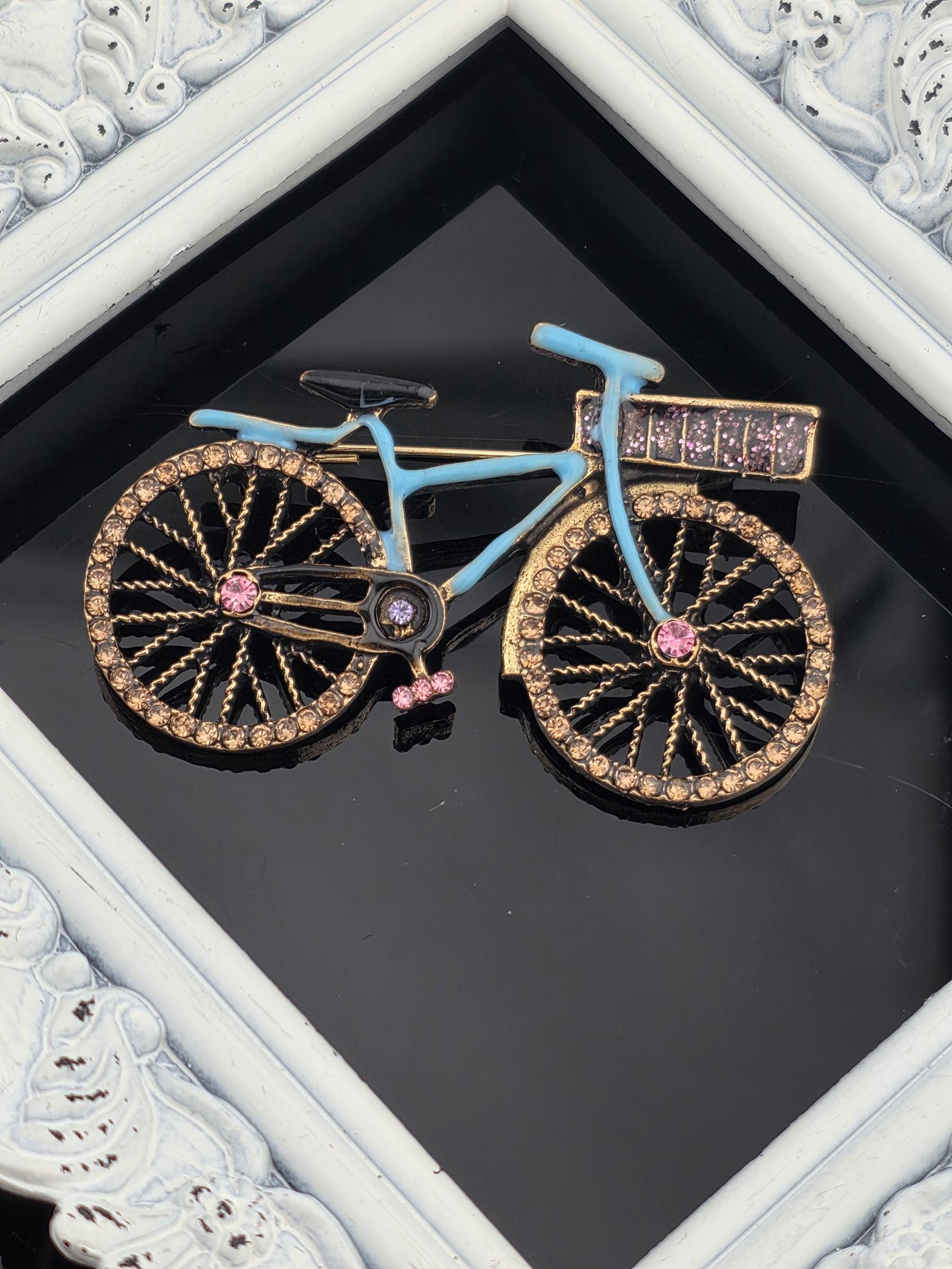 A decorative bicycle with a blue frame and gold accents, including rhinestones, is displayed in a white ornate frame.