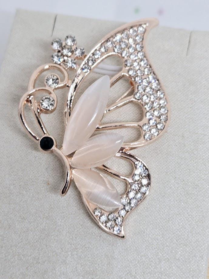 A decorative pin in the shape of a butterfly, adorned with rhinestones and a black gemstone.
