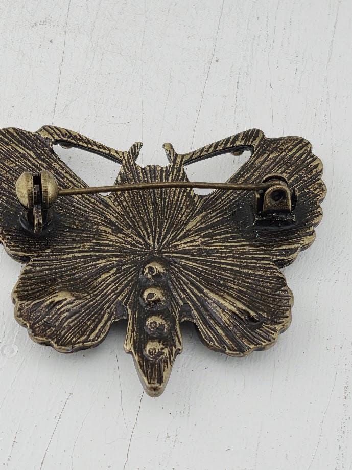 A decorative butterfly brooch with a textured, metallic appearance.