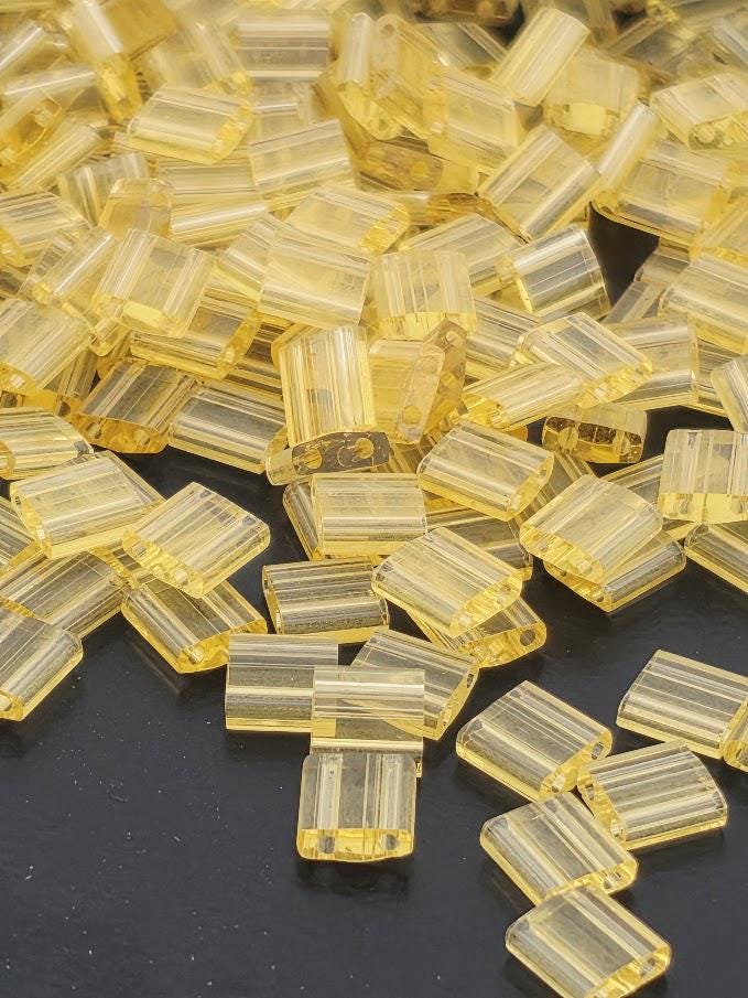 a pile of small, clear plastic beads in various shades of yellow, scattered on a dark surface.