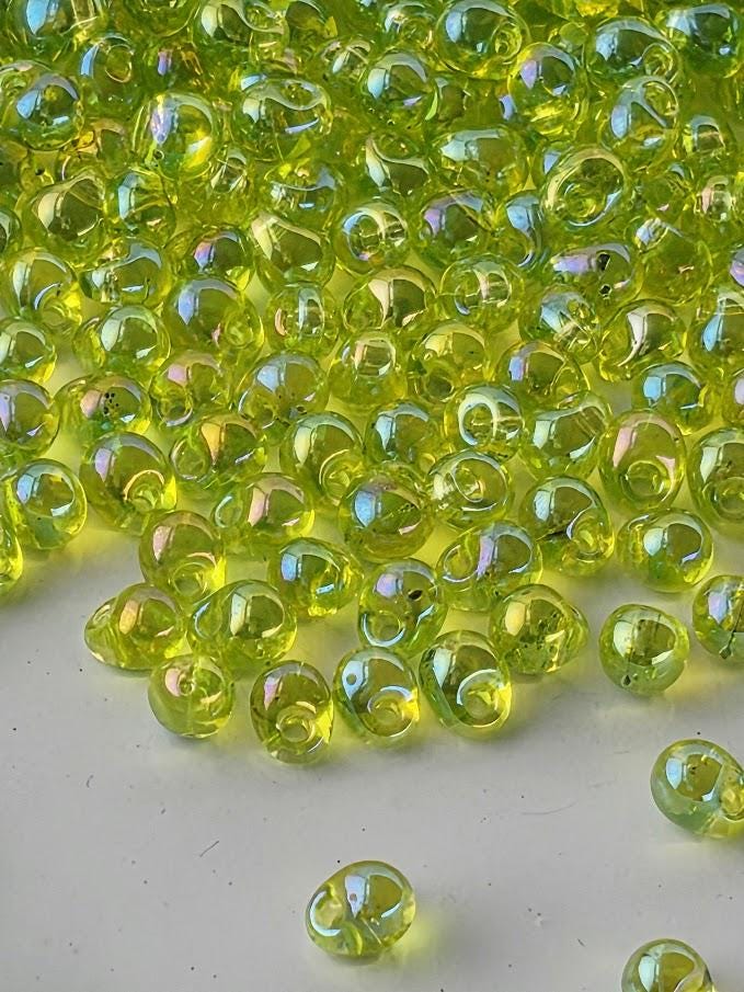a collection of small, clear, and shiny green glass beads scattered on a white surface.