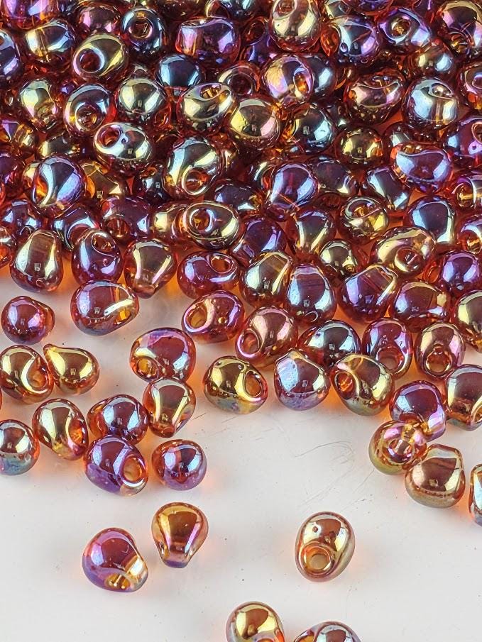 a collection of colorful glass beads scattered on a white surface. The beads come in various shades of orange, purple, and yellow, creating a vibrant and visually appealing display.