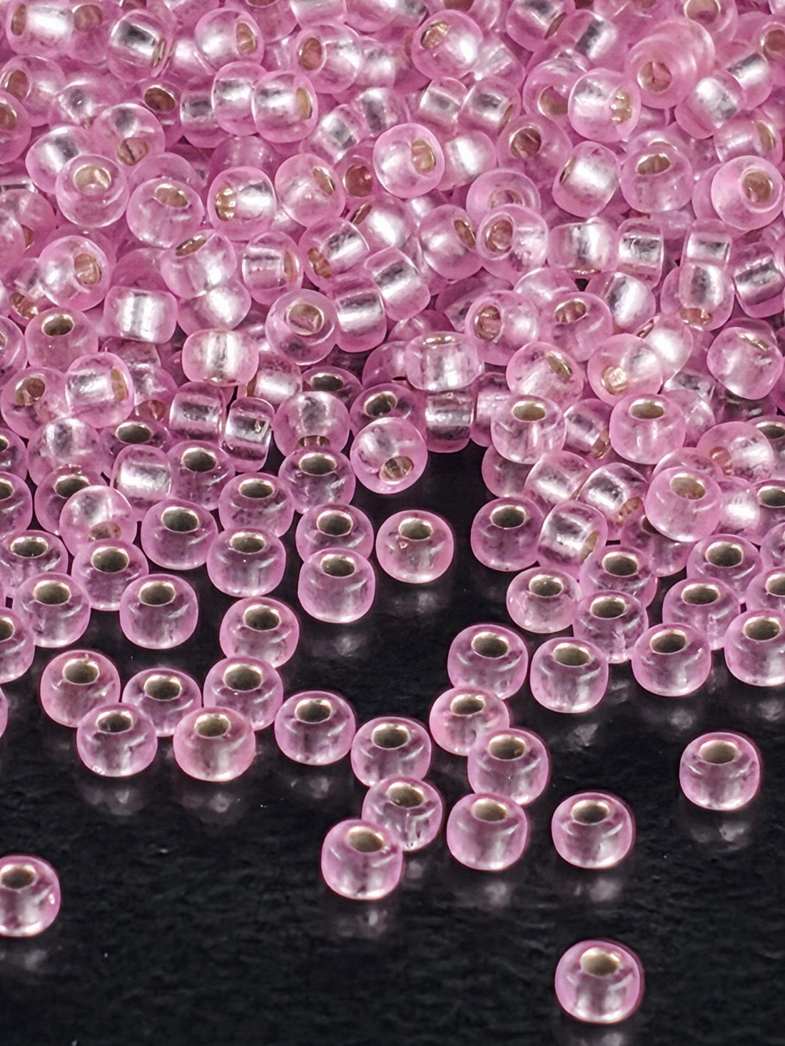 a close-up view of numerous small, clear beads in shades of pink and silver, scattered across a dark background.