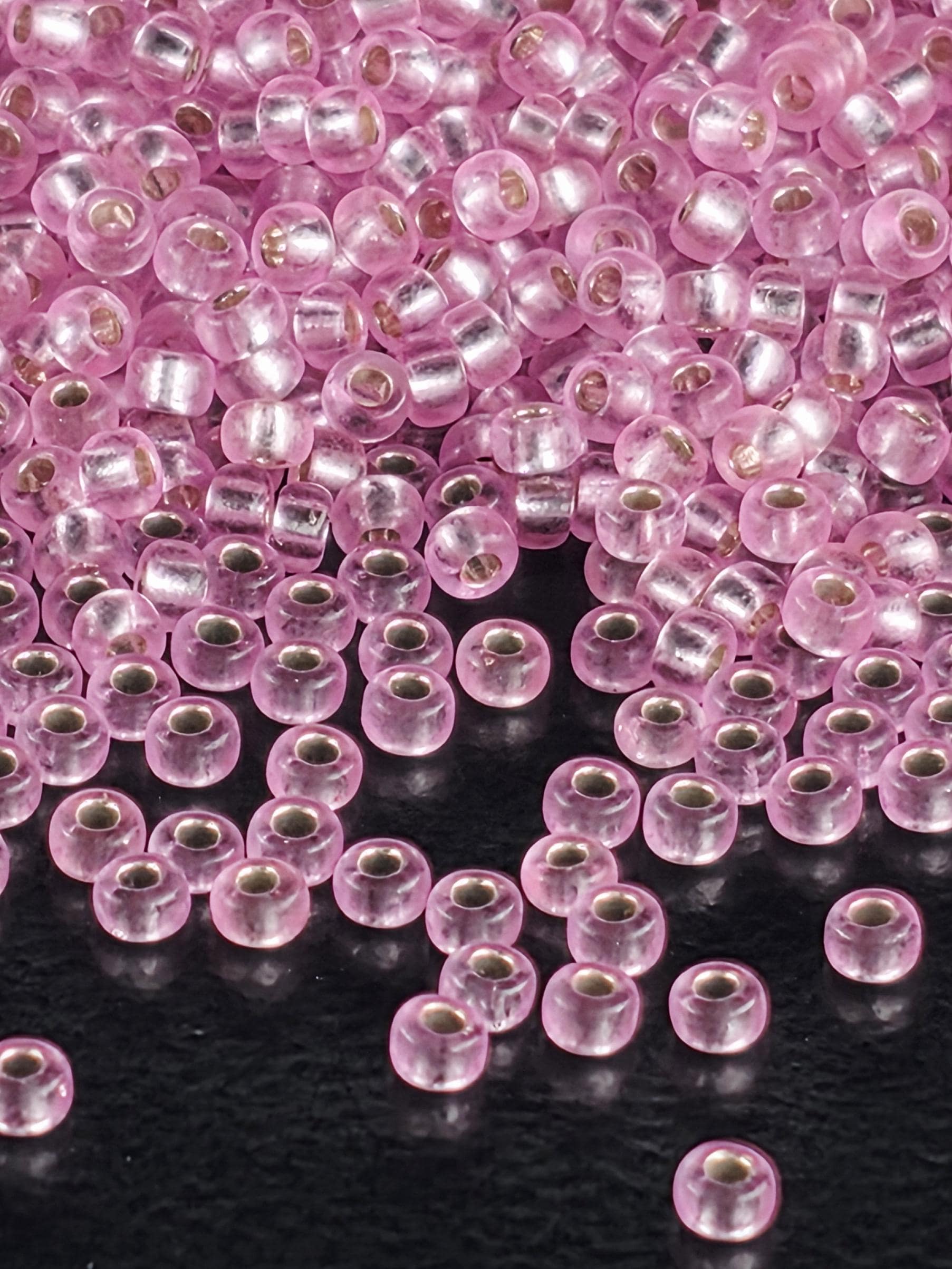 a close-up view of numerous small, clear beads in shades of pink and silver, scattered across a dark background.