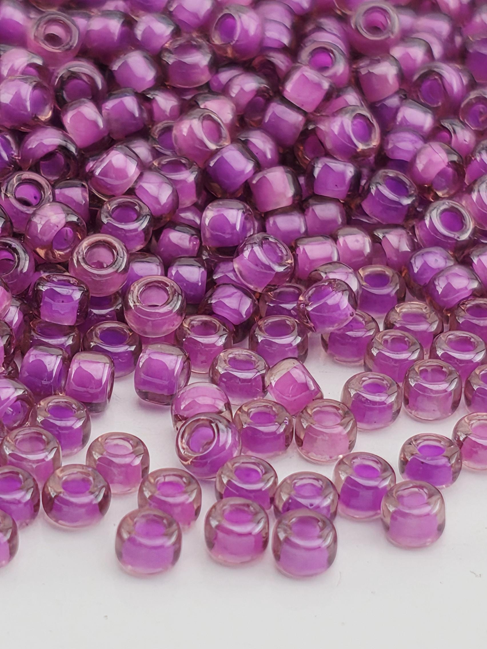 a close-up view of numerous small, clear beads in shades of purple. The beads are scattered across a surface, creating a visually striking and colorful display.