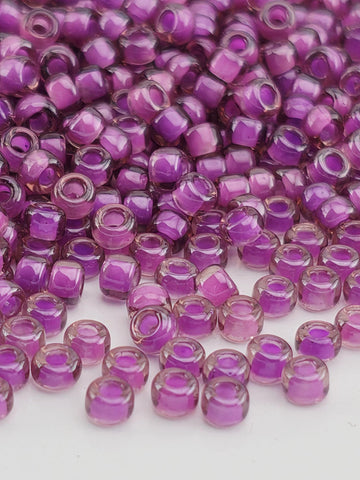 a close-up view of numerous small, clear beads in shades of purple. The beads are scattered across a surface, creating a visually striking and colorful display.