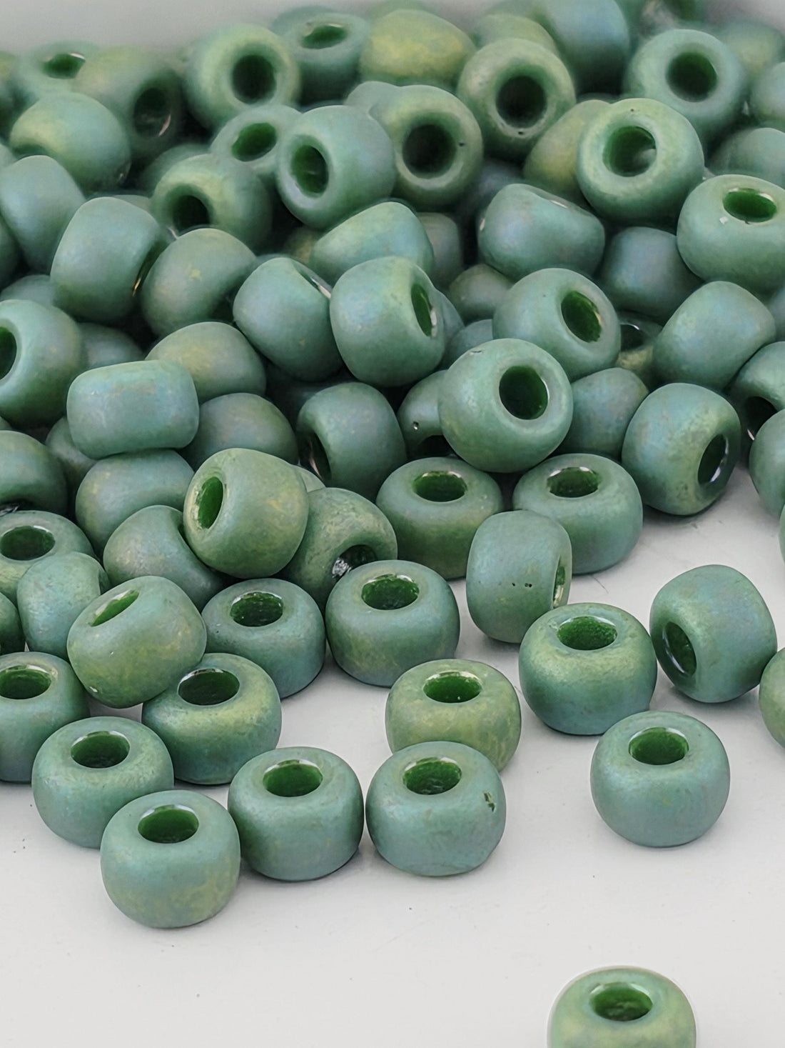 A pile of green glass beads with small holes, scattered on a white surface.