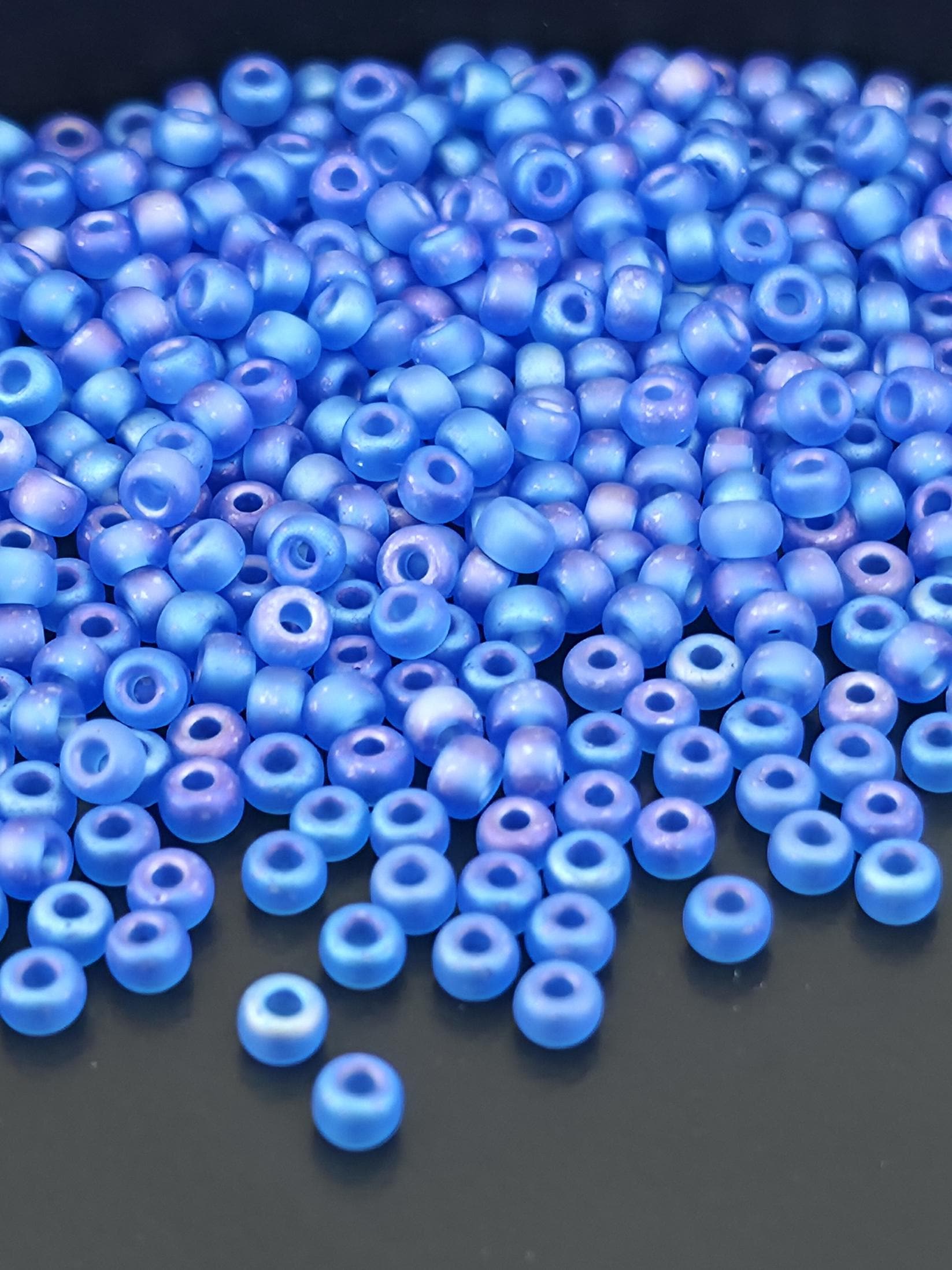A close-up image of numerous blue beads scattered on a dark surface.