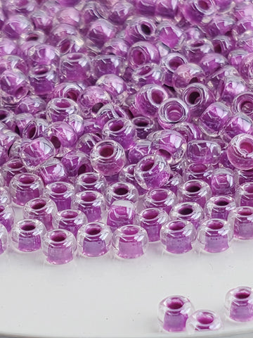 The image is a close-up of numerous clear and purple glass beads arranged in a pattern.