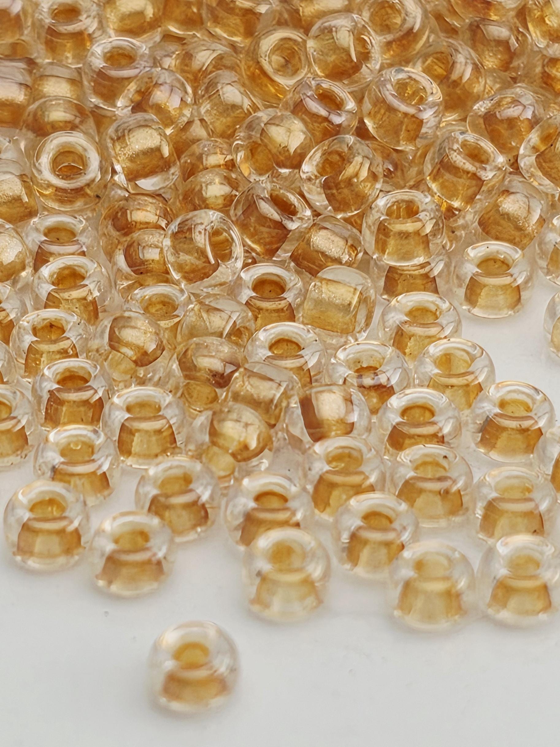 a close-up view of numerous small, clear beads in various shades of gold and yellow, scattered across a white surface.