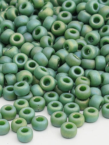 a large pile of green beads or beads with a similar color and shape, scattered on a white surface.