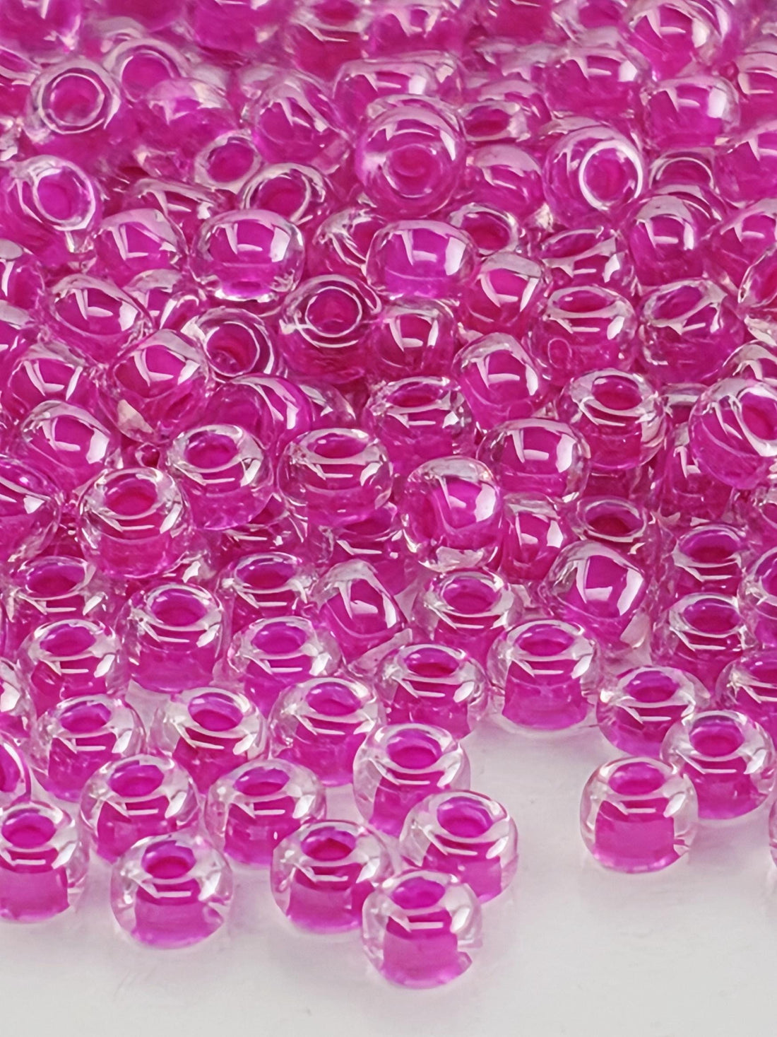 The image is a close-up of numerous clear, round beads in a vibrant shade of pink. The beads are scattered across the frame, creating a visually striking and colorful composition.