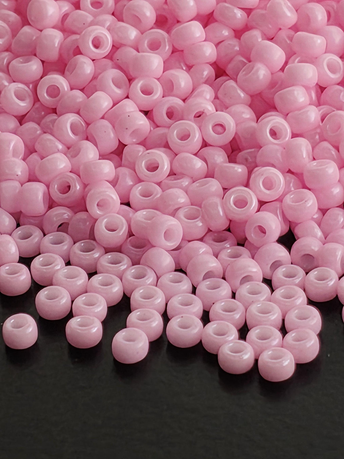 A close-up image of numerous pink beads scattered on a dark background.