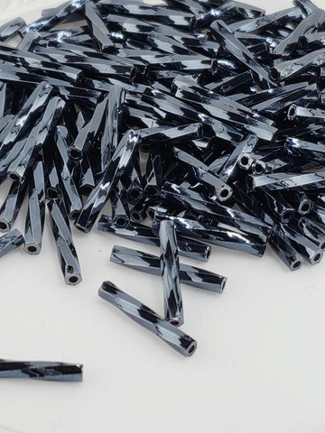 a pile of black, shiny metal rods or rods with a reflective surface, scattered on a white background.