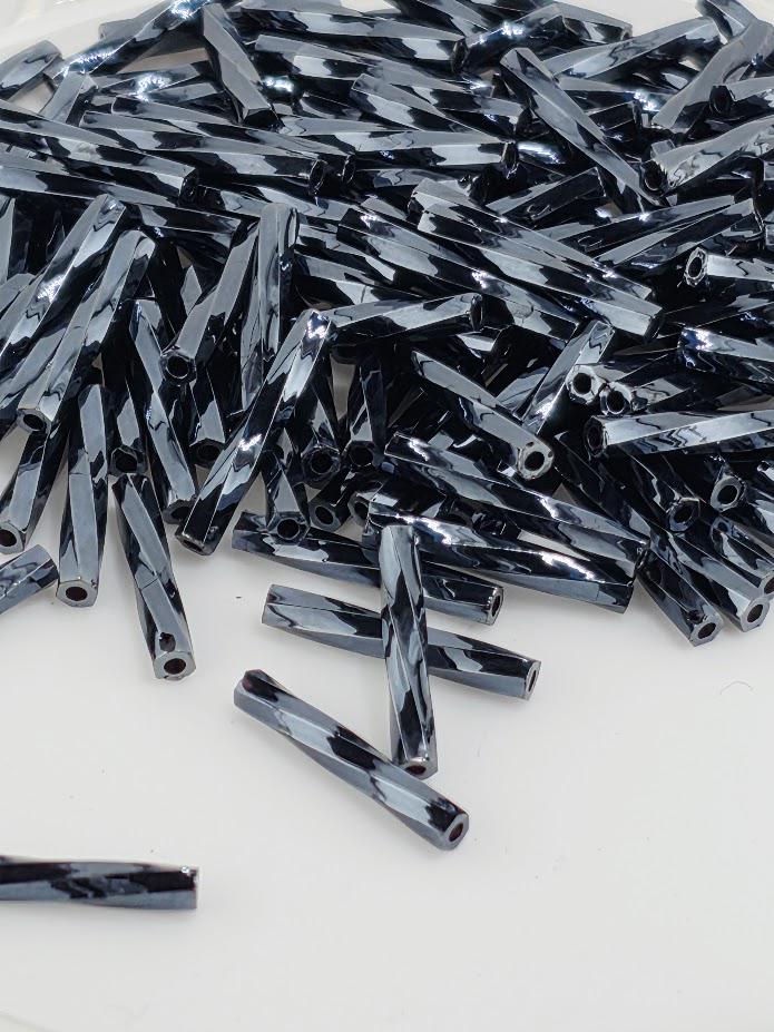 a pile of black, shiny metal rods or rods with a reflective surface, scattered on a white background.