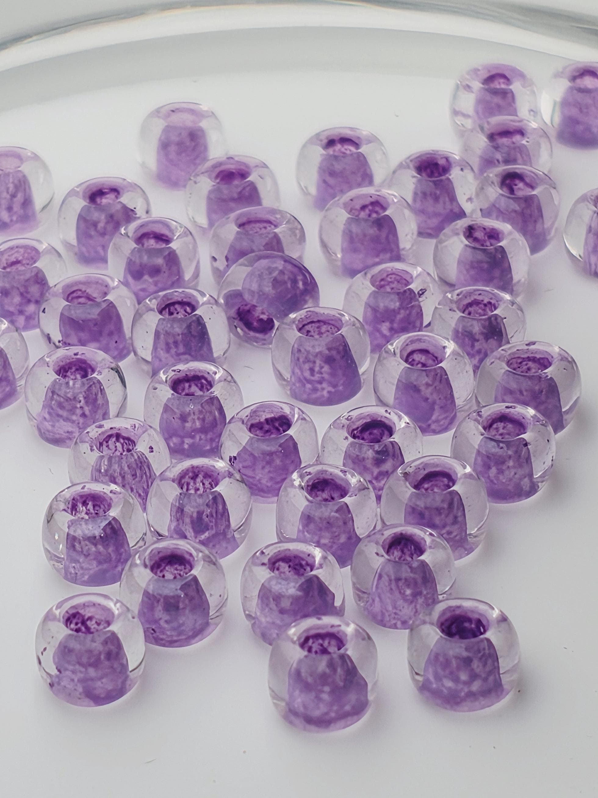 a collection of clear glass beads with purple and white colors, scattered across a white surface.