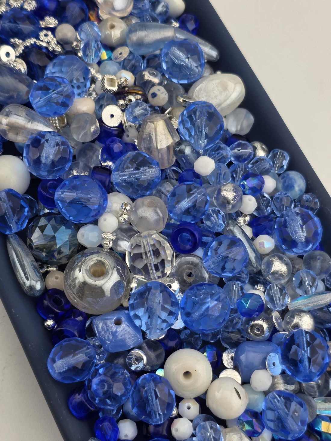 a variety of blue and silver glass beads, including clear, blue, and silver beads, as well as some white beads. The beads are scattered throughout the frame, creating a visually interesting and diverse collection.