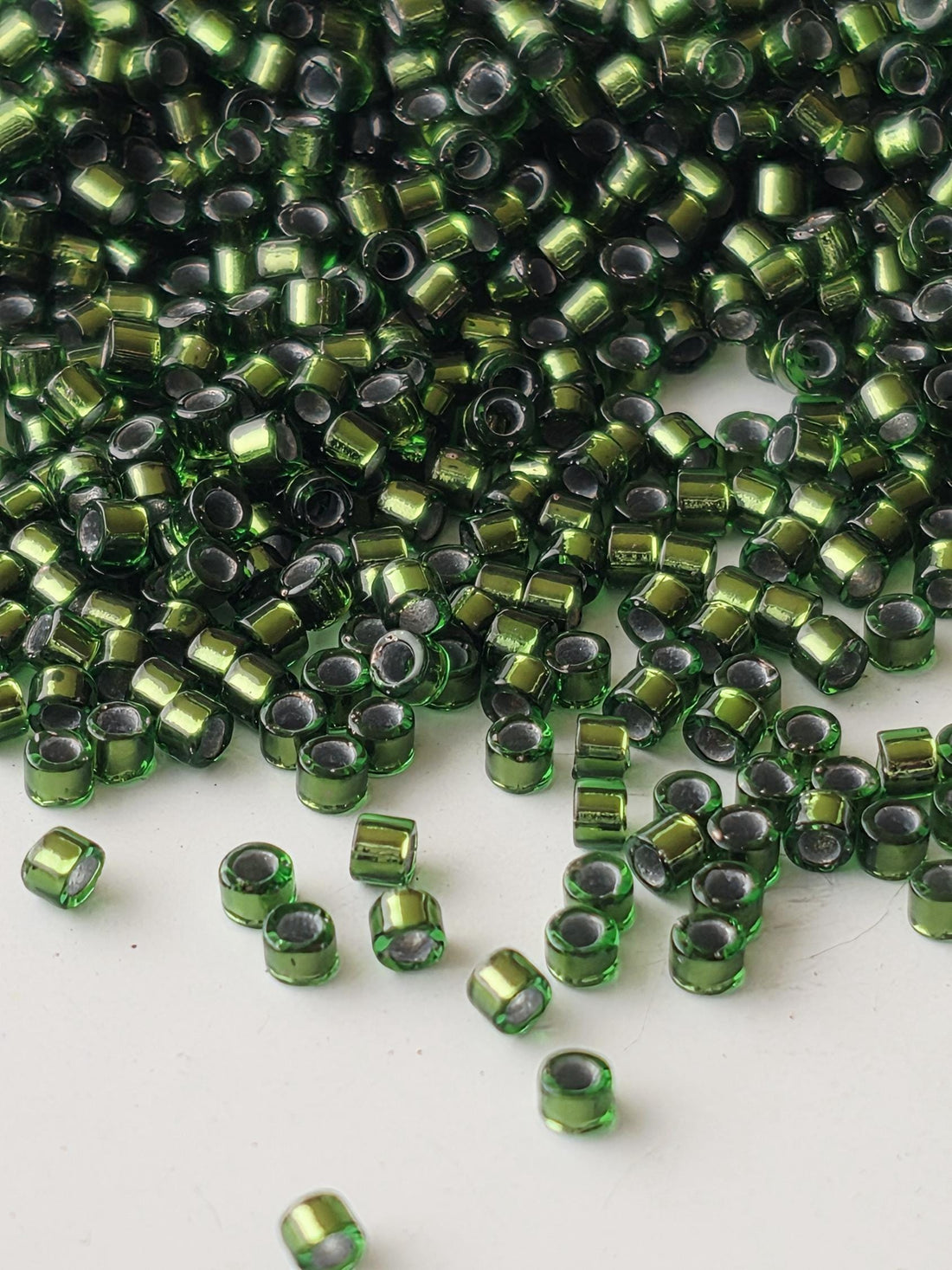 a large pile of green and silver beads scattered on a white surface.
