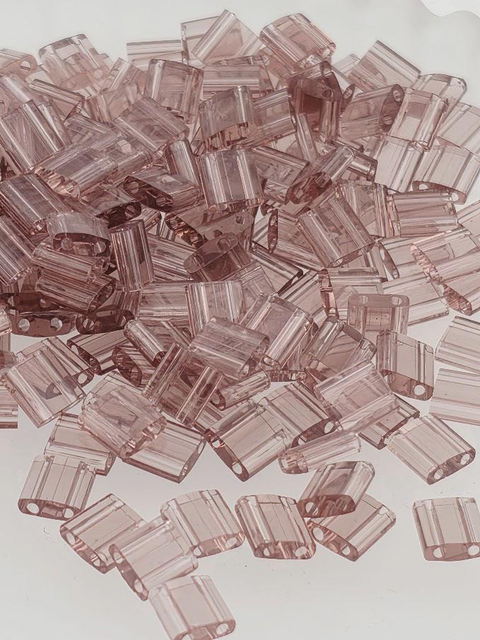 numerous small, clear plastic beads in various shades of pink, scattered across a white background.
