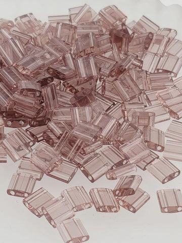 numerous small, clear plastic beads in various shades of pink, scattered across a white background.