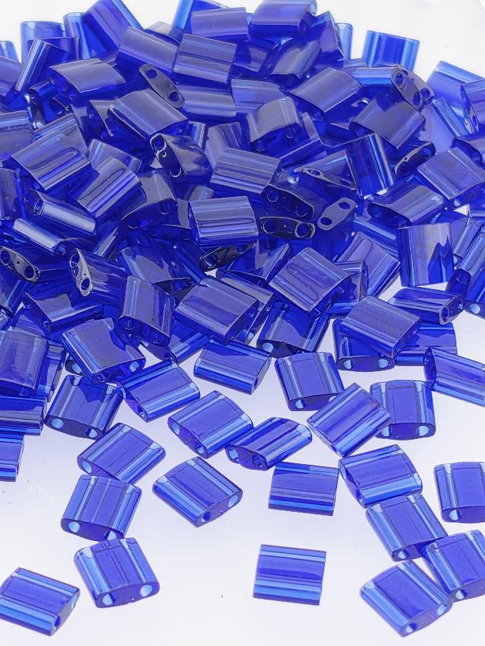 The image is a collection of numerous blue glass beads or beads, scattered and overlapping each other in various shapes and sizes.