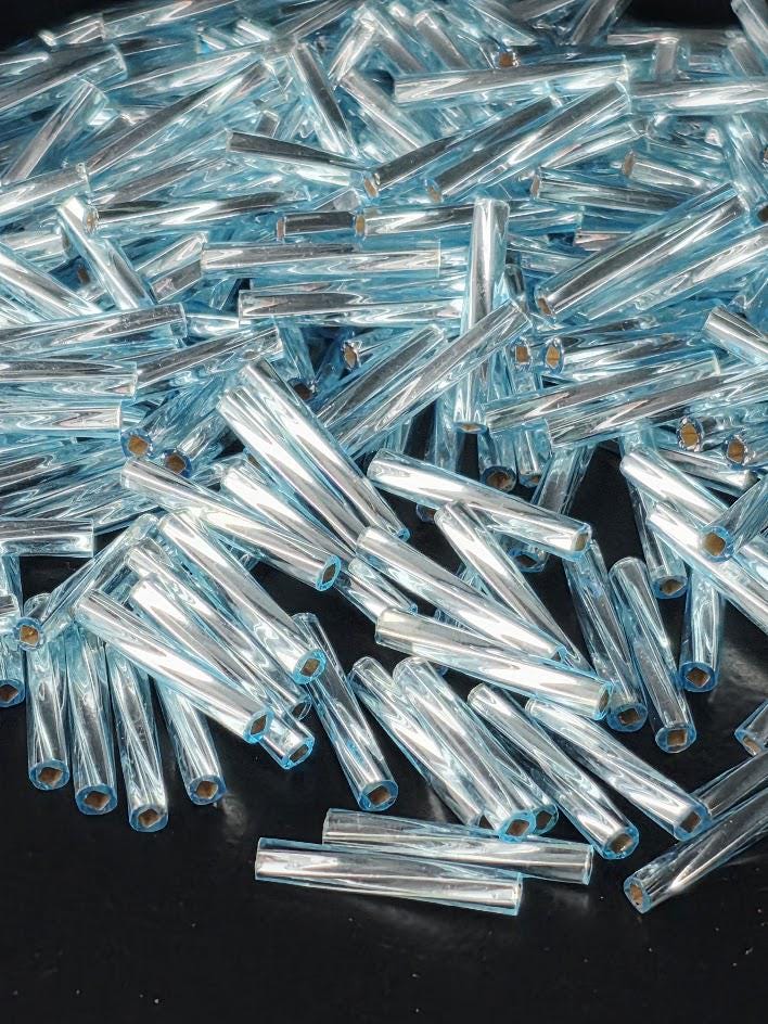 The image is a close-up of numerous blue glass rods or tubes scattered on a dark surface.