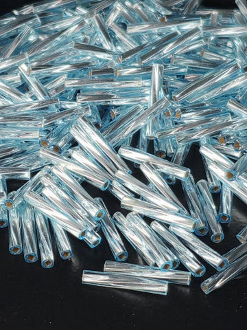 The image is a close-up of numerous blue glass rods or tubes scattered on a dark surface.