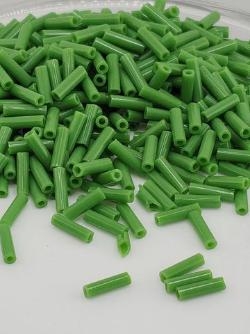 a pile of green, cylindrical objects, possibly beads or small tubes, scattered on a white surface.