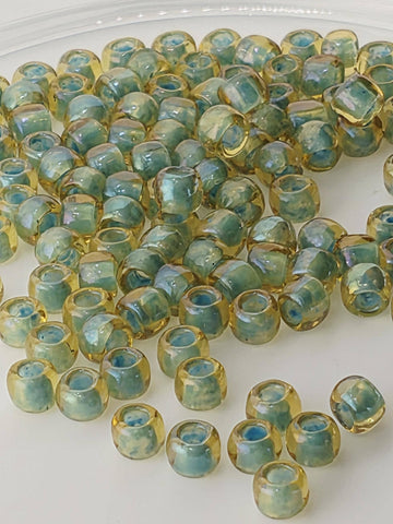 a collection of small, clear beads in various shades of green and yellow, scattered on a white surface.