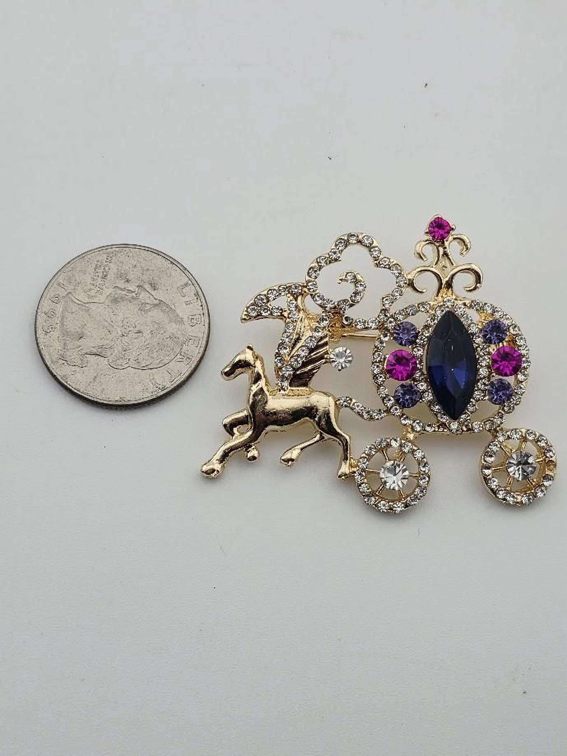 A small gold-colored pin with a unicorn and gemstone design, placed next to a silver coin for scale.