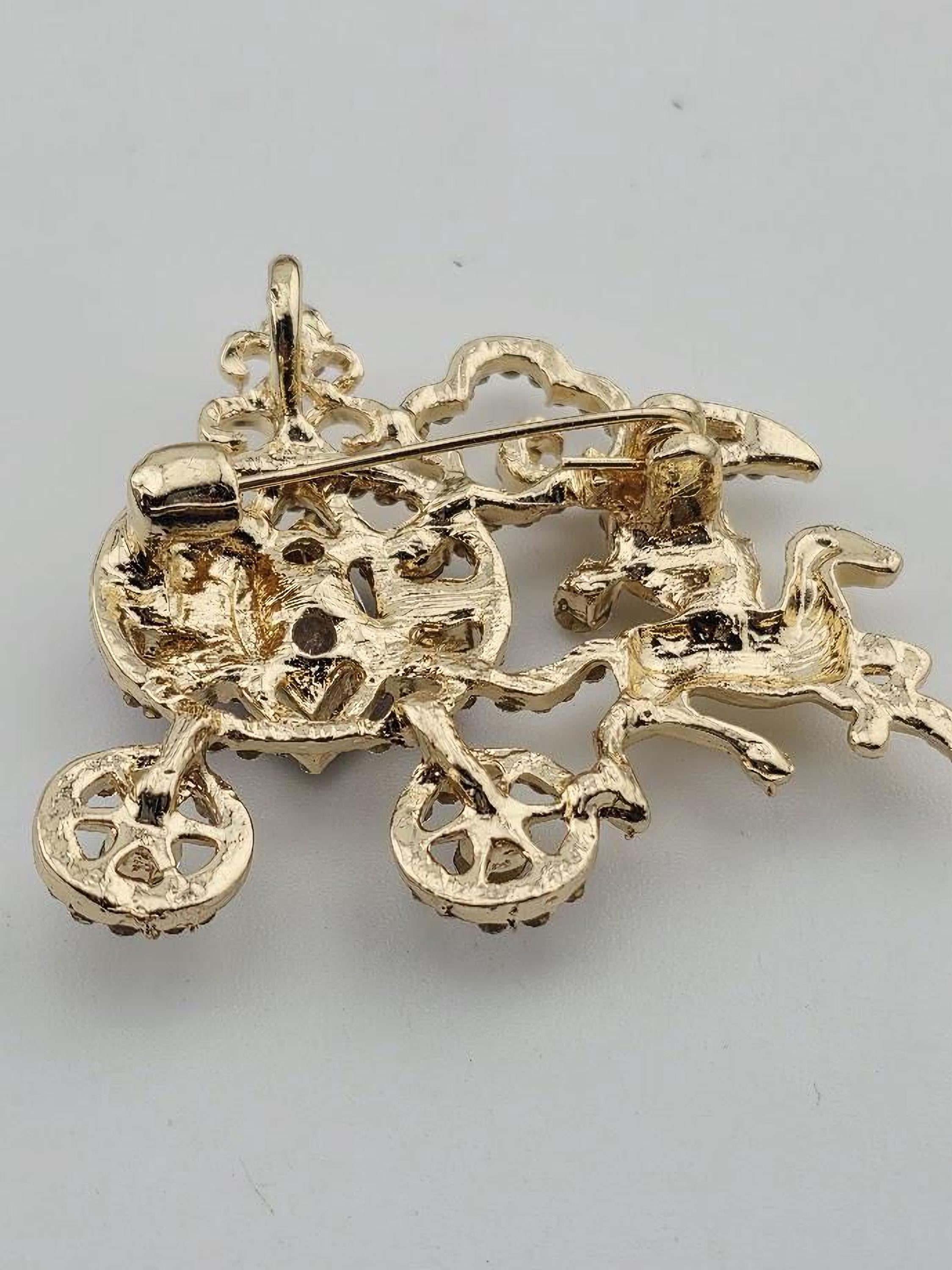 A gold-colored pin or brooch with an intricate design, featuring a bicycle-like structure with wheels and a handlebar.