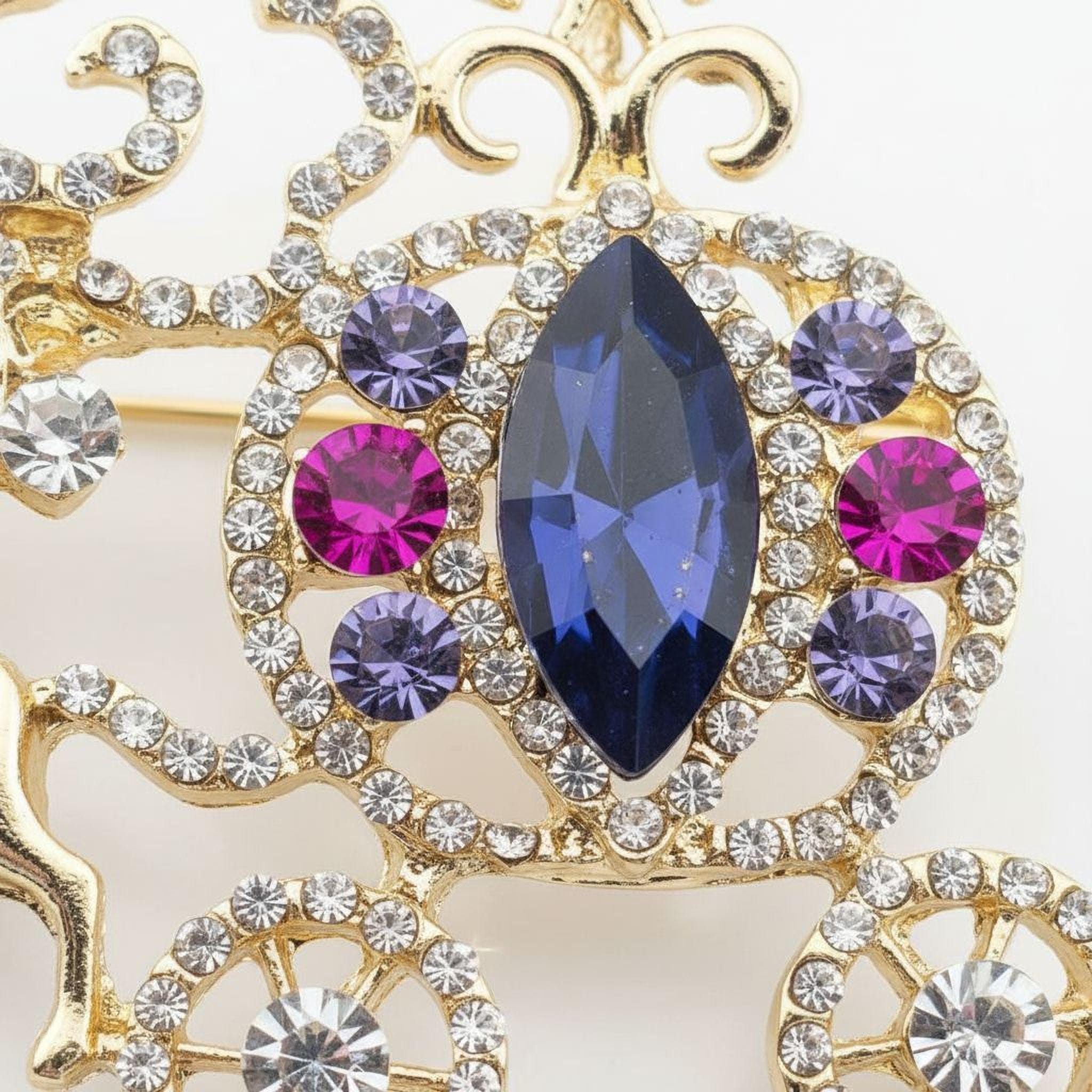 a close-up view of a decorative piece, possibly a brooch or necklace, adorned with a variety of colorful gemstones. The piece is intricately designed and showcases a striking combination of blue, purple, and pink gemstones, all set against a gold background.