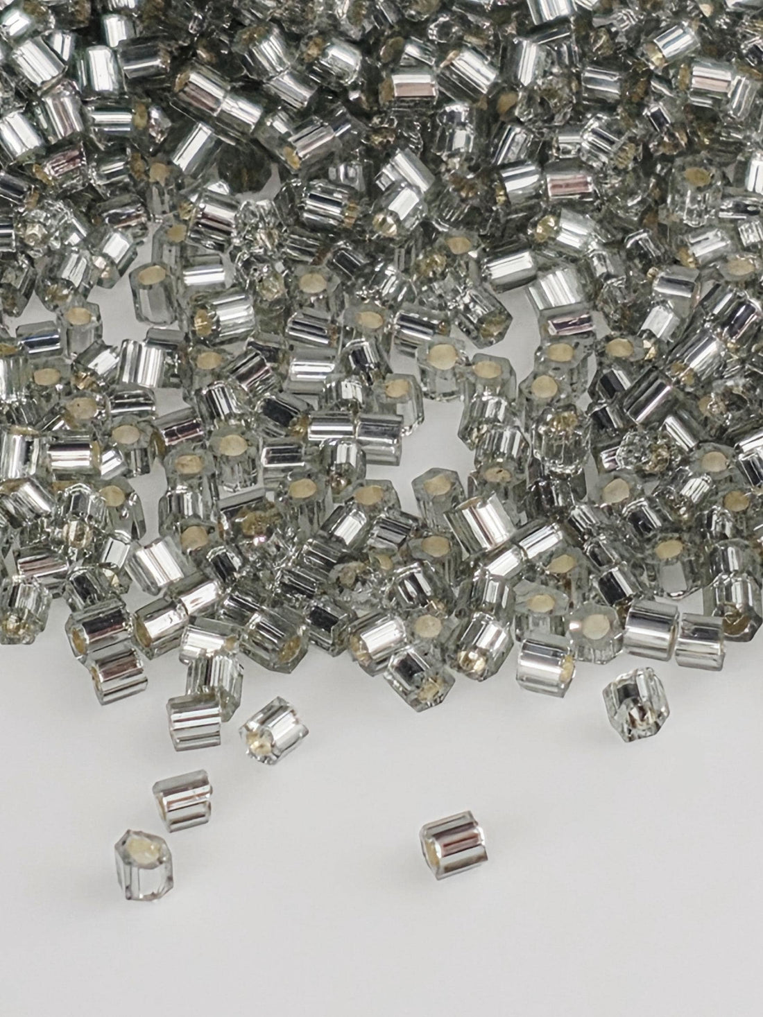 The image is a close-up of numerous silver and white beads or crystals, scattered and overlapping each other.