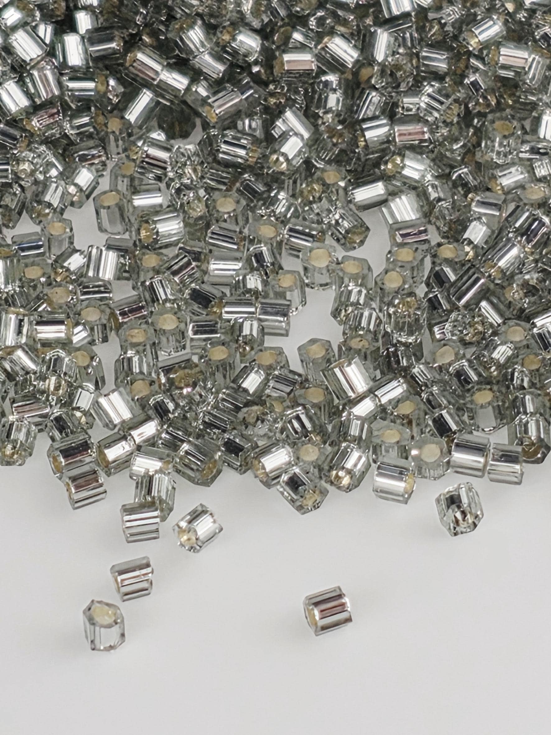The image is a close-up of numerous silver and white beads or crystals, scattered and overlapping each other.