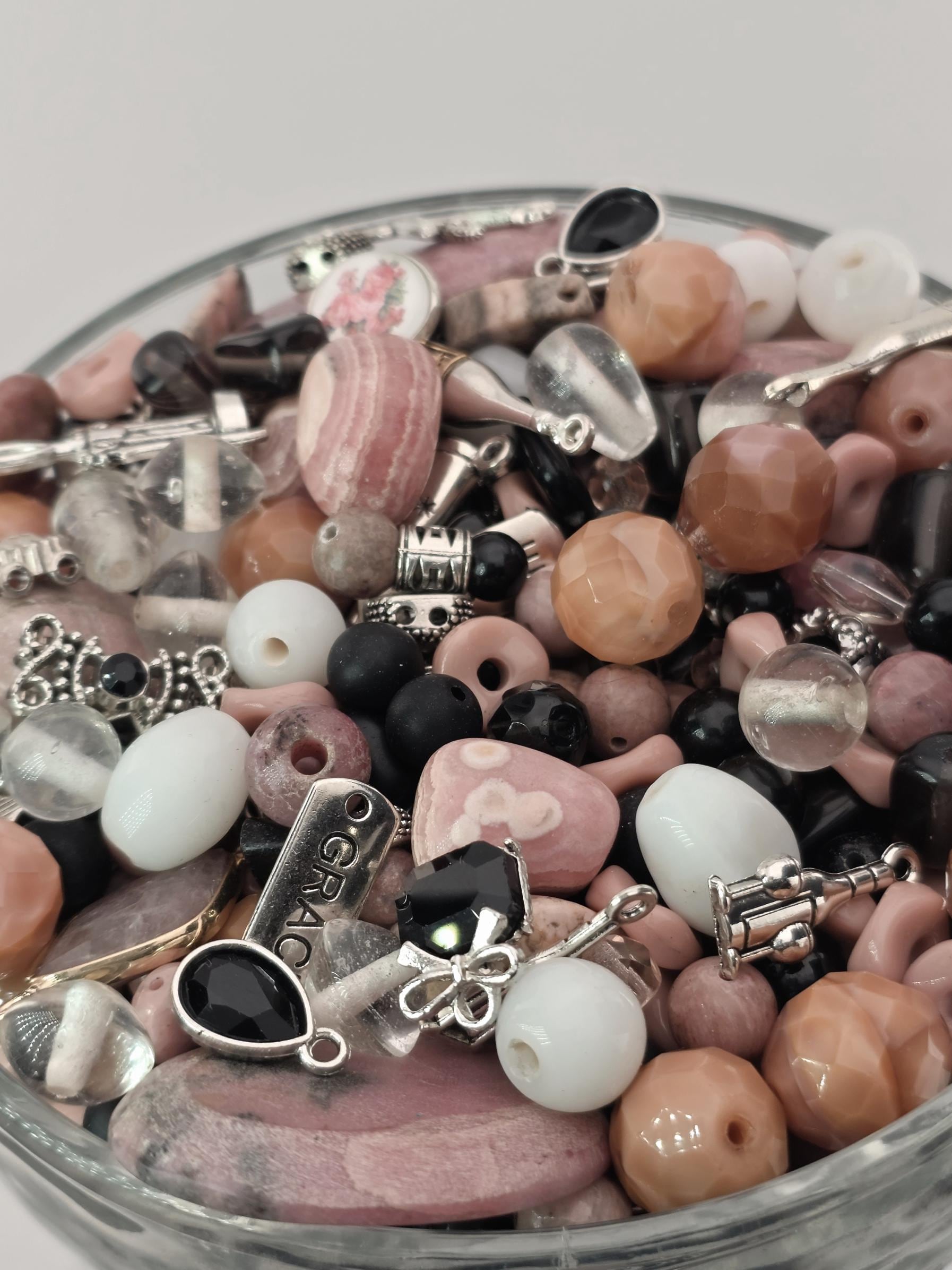 A close-up view of a collection of various beads, charms, and other decorative items arranged in a glass container.