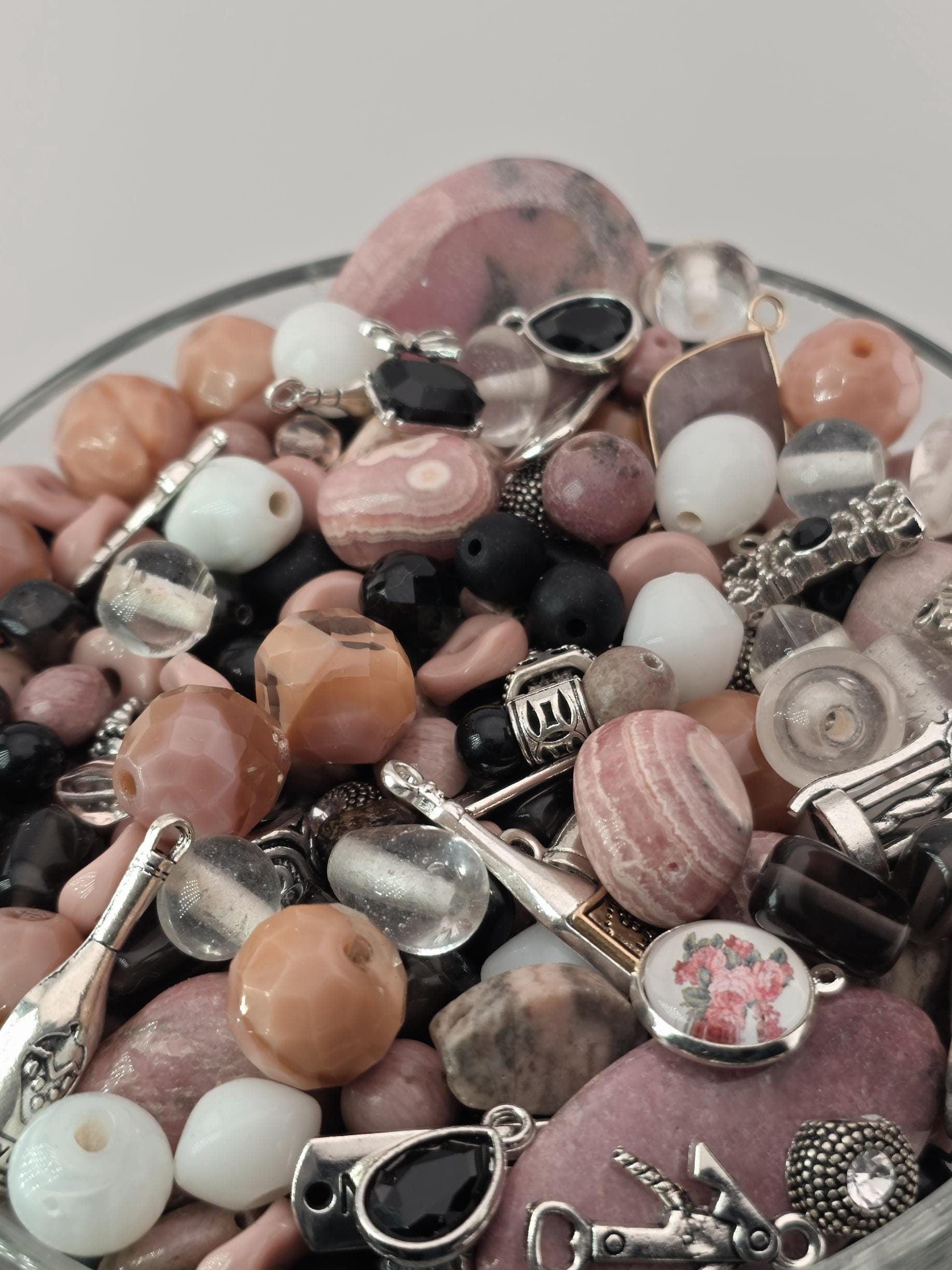 A close-up image of various beads, charms, and other decorative items arranged in a glass container.